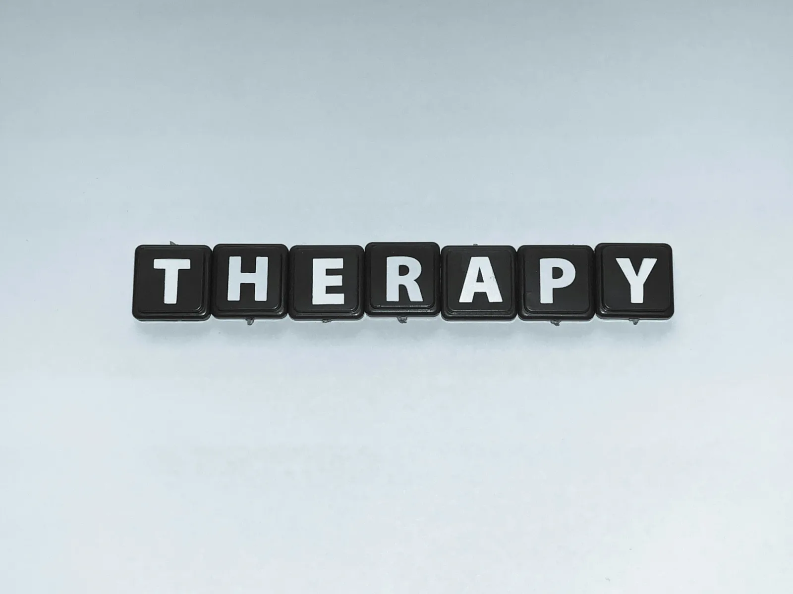 Cuvântul „therapy" format din litere albe pe pătrățele negre, aliniate orizontal pe un fundal alb-albastru minimalist